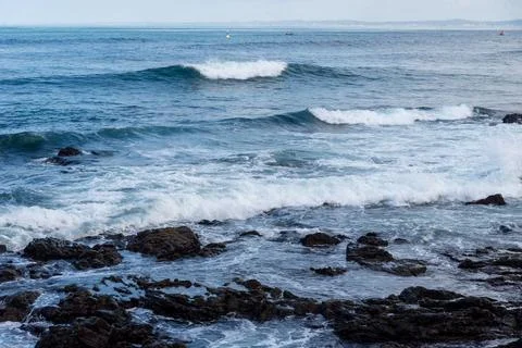 Waves breaking against dark rocks in the sea Stock Photos