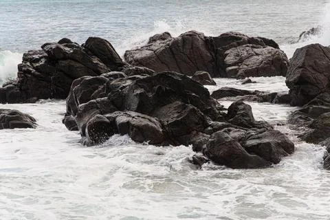 Waves breaking against dark rocks Stock Photos