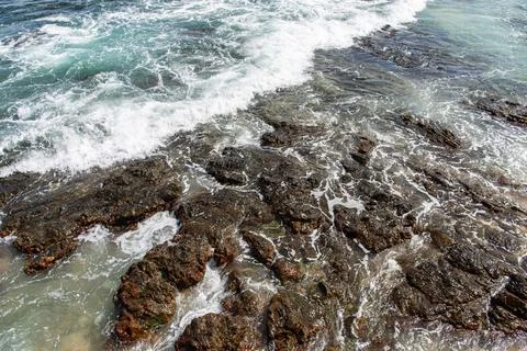 Waves breaking against dark rocks in the sea Stock Photos
