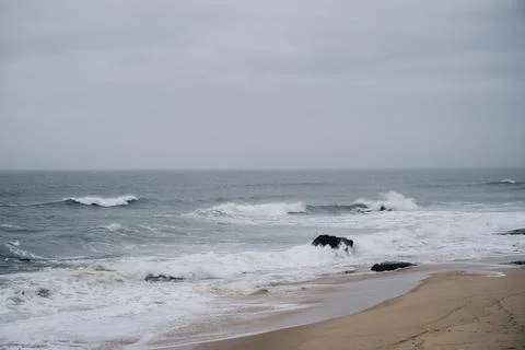 Waves breaking along sandy beach under cloudy sky in Santa Cruz Portugal Stock Photos