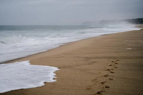 Waves breaking along sandy beach under cloudy sky in Santa Cruz Portugal Foto stock