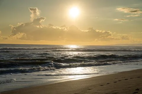 Waves breaking on beach with evening sun and clouds Foto stock