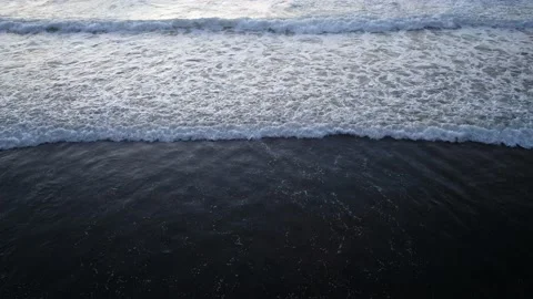Waves breaking over a black sand beach in slow motion Video stock 231592657