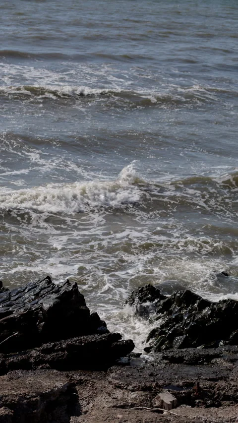 Waves Breaking Over Dark Coastal Rocks Along Gritty Shoreline in Gray Open Water Stock Footage 346559009