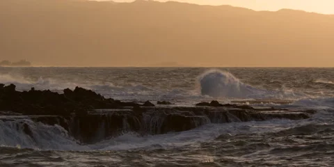 Waves breaking over a rocky reef with  glowing Hawaiian hills beyond Stock Footage 59525683