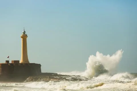 Waves breaking on the rocks and the lighthouse Stock Photos