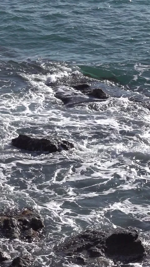 Waves breaking on rocks in bright sunlight, high contrast, vertical view Video stock 332610485