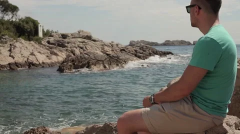 Waves breaking the rocks. Young man with mobile phone. Video stock 53606795