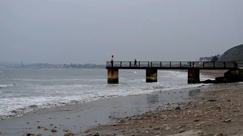 Waves breaking onto sand at Bowleaze Cove - people on pier Stock Footage 106094045