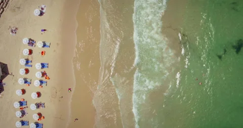 Waves breaking onto a sandy shore by a lifeguard stand and sun umbrellas aeri Stock Footage 275582382