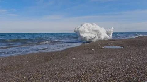 Waves breaking on shore by lump of white ice on a sandy beach Stock Footage 245040991