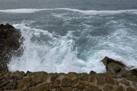 Waves breaking on the shore on a pebble road Stock Photos
