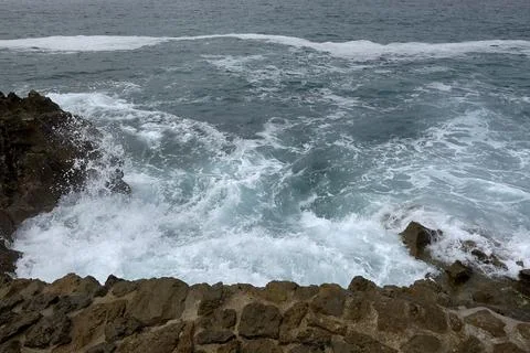 Waves breaking on the shore on a pebble road Stock Photos