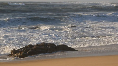 Waves breaking on the shore of a sandy beach with rock to left of frame Stock Footage 103277309