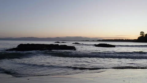 Waves breaking on shore as sun sets over mountains Stock Footage 260370631