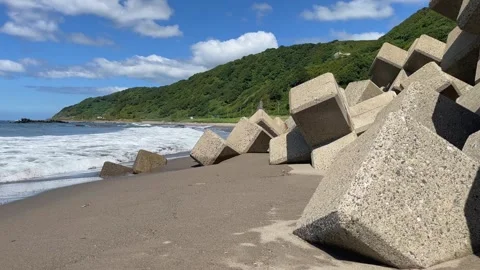 Waves breaking by tetrapods lining a sandy beach on a summer day Stock Footage 247896999