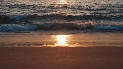 Waves calmly washing on sandy beach while the sun sets on behind Stock Footage 119110509