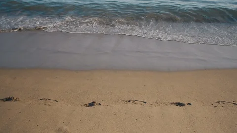 Waves calmly washing on sandy beach with foot tracks Stock Footage 119116751