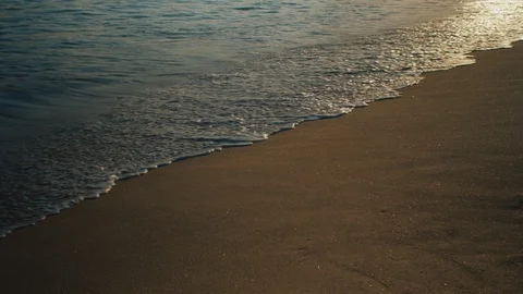 Waves calmly washing on a sandy beach with afternoon sun reflection Stock Footage 119119294