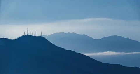Waves of clouds flowing between mountains over a blue sky during sunset Stock Footage 138329509