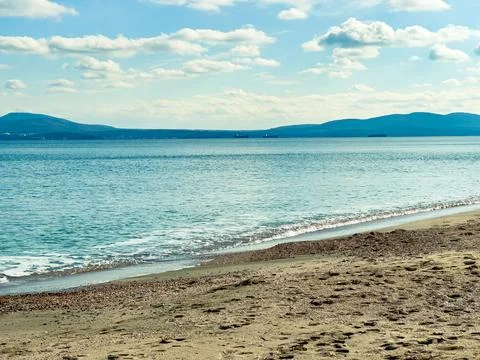 Waves come ashore on a sandy beach while ships float on the water in the dist Stock Photos