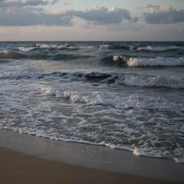 Waves coming to a beach with clouds above Stockfoto's