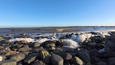Waves cover pebble beach shoreline under paradise blue cloudless sky 動画素材 324964707