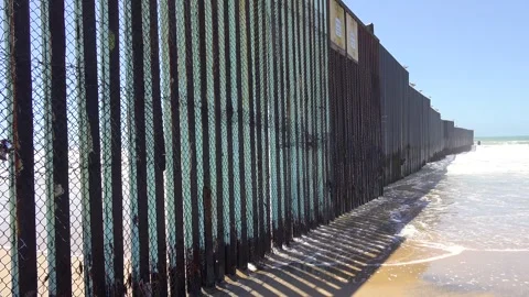 Waves crash against border fence dividing usa and mexico, beach is visible .. Vídeo Stock 337760660