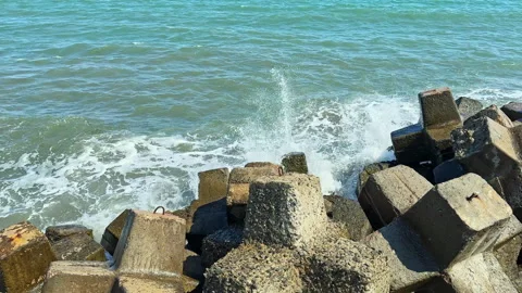 Waves crash against concrete blocks by the shore on a sunny day near the water Stock Footage 344786351