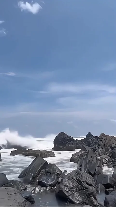 Waves crash against rocks at beach, sea spray in air, sunlight reflects on water Stock Footage 318074601