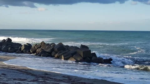 Waves Crash Against Rocks on a Serene Beach During the Afternoon Under a Partly Stock Footage 306592779