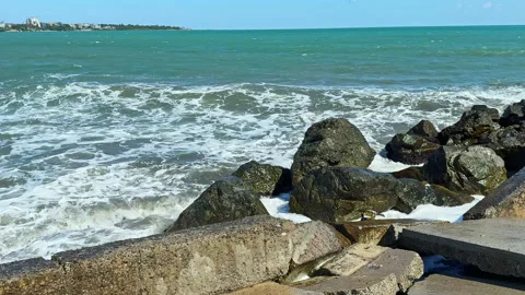 Waves crash against rocks by the shore during a bright day in a coastal area Stock Footage 344786031