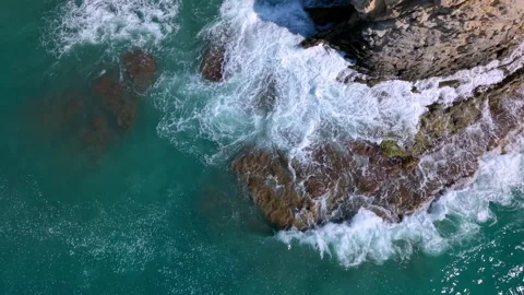Waves crash against rocks at the shore under bright sunlight in a scenic Stock Footage 346017631
