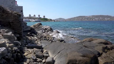 Waves Crash Against Rocks with Windmills of Mykonos Greece Wide View Across.. Stock Footage 336512943