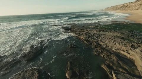 Waves crash against rocky cliffs and sandy shore Stock Footage 341826950