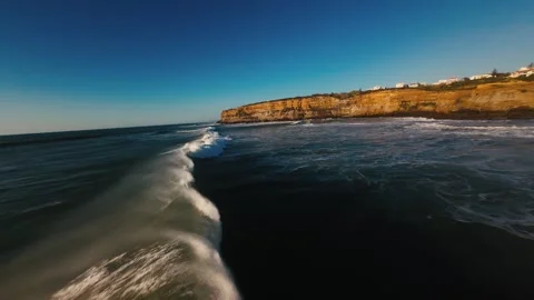 Waves crash against rugged cliffs under clear blue sky Stock Footage 339787707