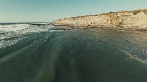 Waves crash against rugged cliffs under clear blue sky Stock Footage 339791442