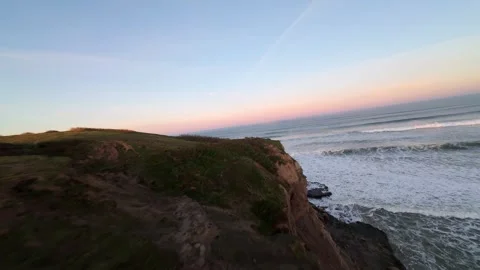 Waves crash against rugged cliffs as sun sets over ocean 库存影片 346158111