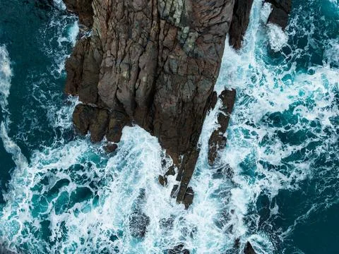 Waves crash against rugged cliffs under the bright sunlight of a clear day by Foto stock