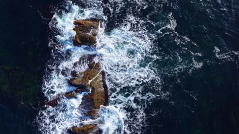 Waves crash against rugged rocks, creating a mesmerizing dance of foam and water Stock Footage 331984508