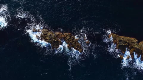 Waves crash against rugged rocks under a vast sky, capturing nature's beauty in Stock Footage 335409492