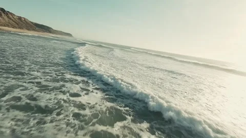 Waves crash against rugged rocks, splashing over sandy shores Stock Footage 341826694