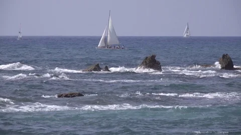 Waves crash against sharp rocks near sail boat Stock Footage 83717455
