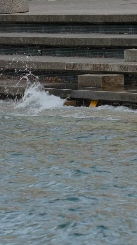 Waves crash against the steps at a waterfront area during a cloudy afternoon in Stock Footage 320304003
