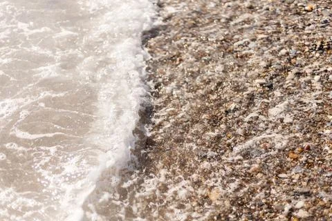 Waves crash onto a beach covered in small stones and pebbles. The water moves Stock Photos