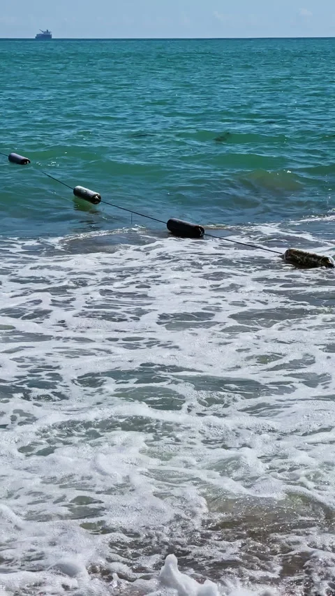 Waves crash on the beach with floating objects in the water on a sunny day Stock Footage 346981697