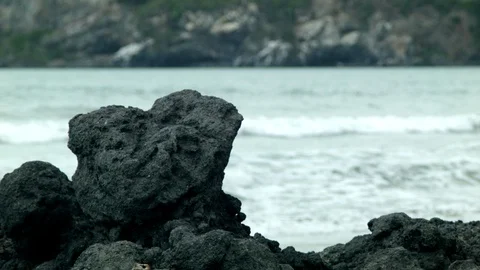 Waves crash behind volcanic rock on the beach Stock Footage 89702157