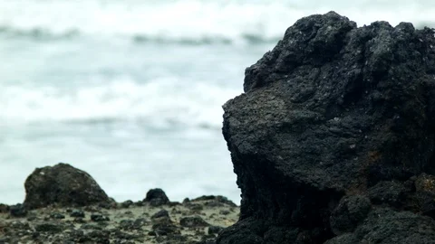 Waves crash behind volcanic rock on the beach Stock Footage 89702206