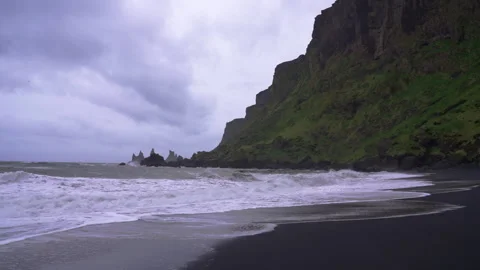Waves crash on black sand beach in Vik, Iceland near towering mountains 스톡 동영상 327082507