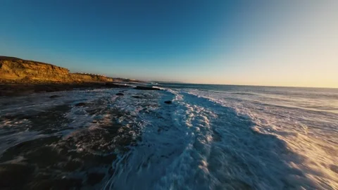 Waves crash on dark, rocky shore under golden sky Stock Footage 339788489